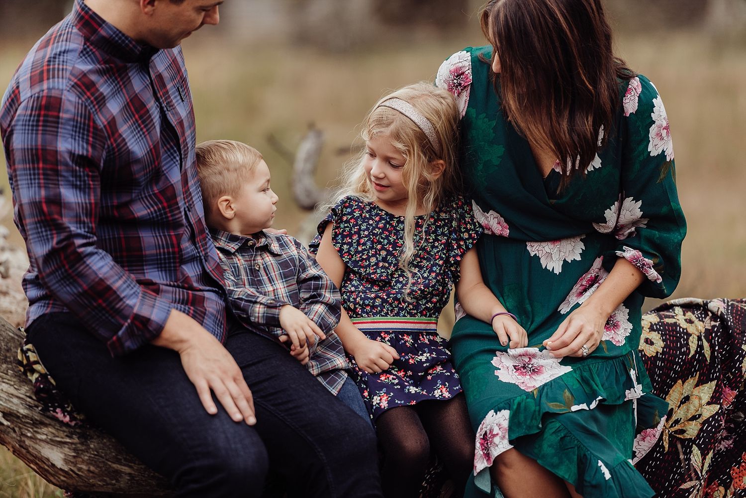 Family sits together on rustic log bench having intimate outdoor conversation.