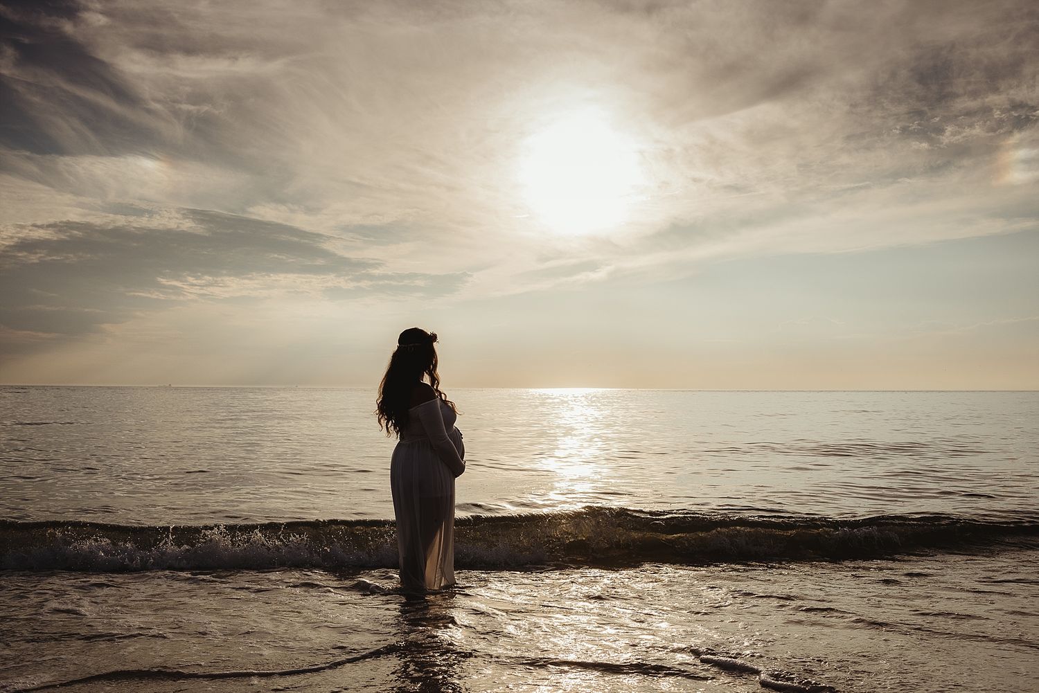 Silhouette of person standing in ocean water during dramatic sunset.