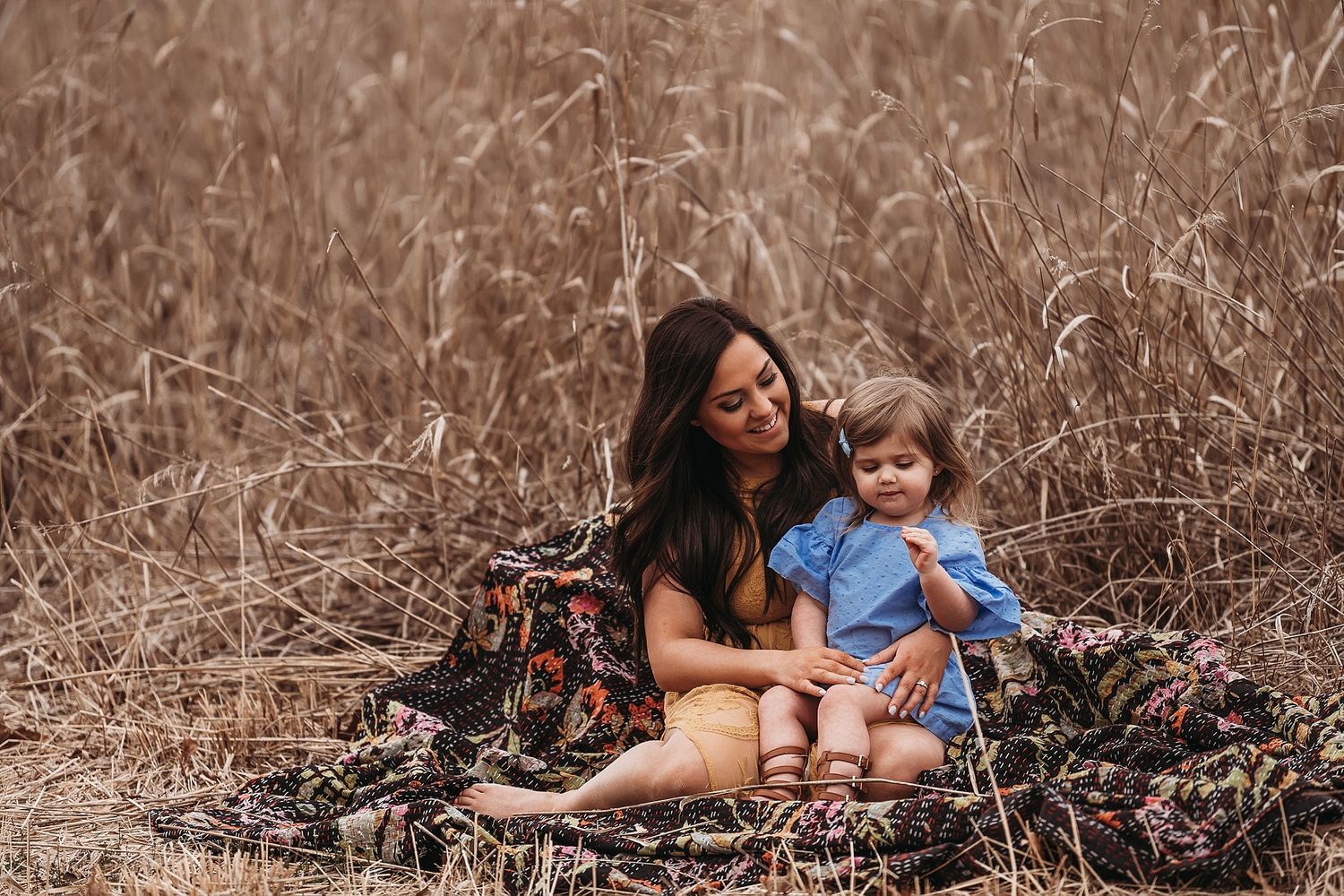 Mother and child share tender moment while sitting on blanket in autumn field.