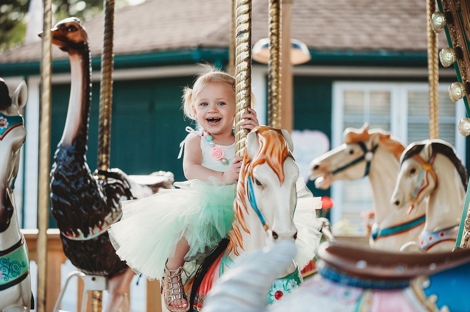 Smiling child in tutu rides colorful carousel horse at amusement park.