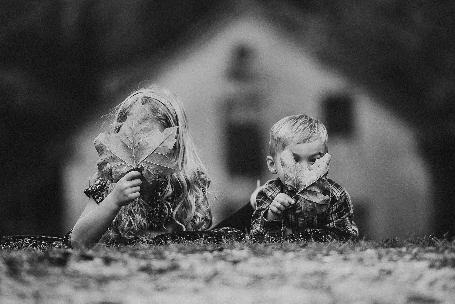Two children looking through binoculars in black and white with a house in the background.