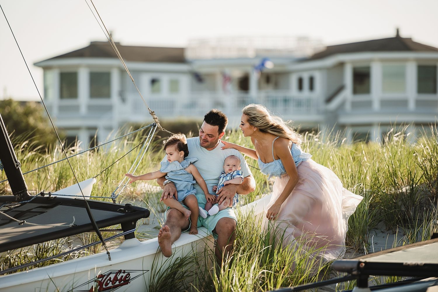 A family shares a joyful moment together near a sailboat in coastal beach grass.