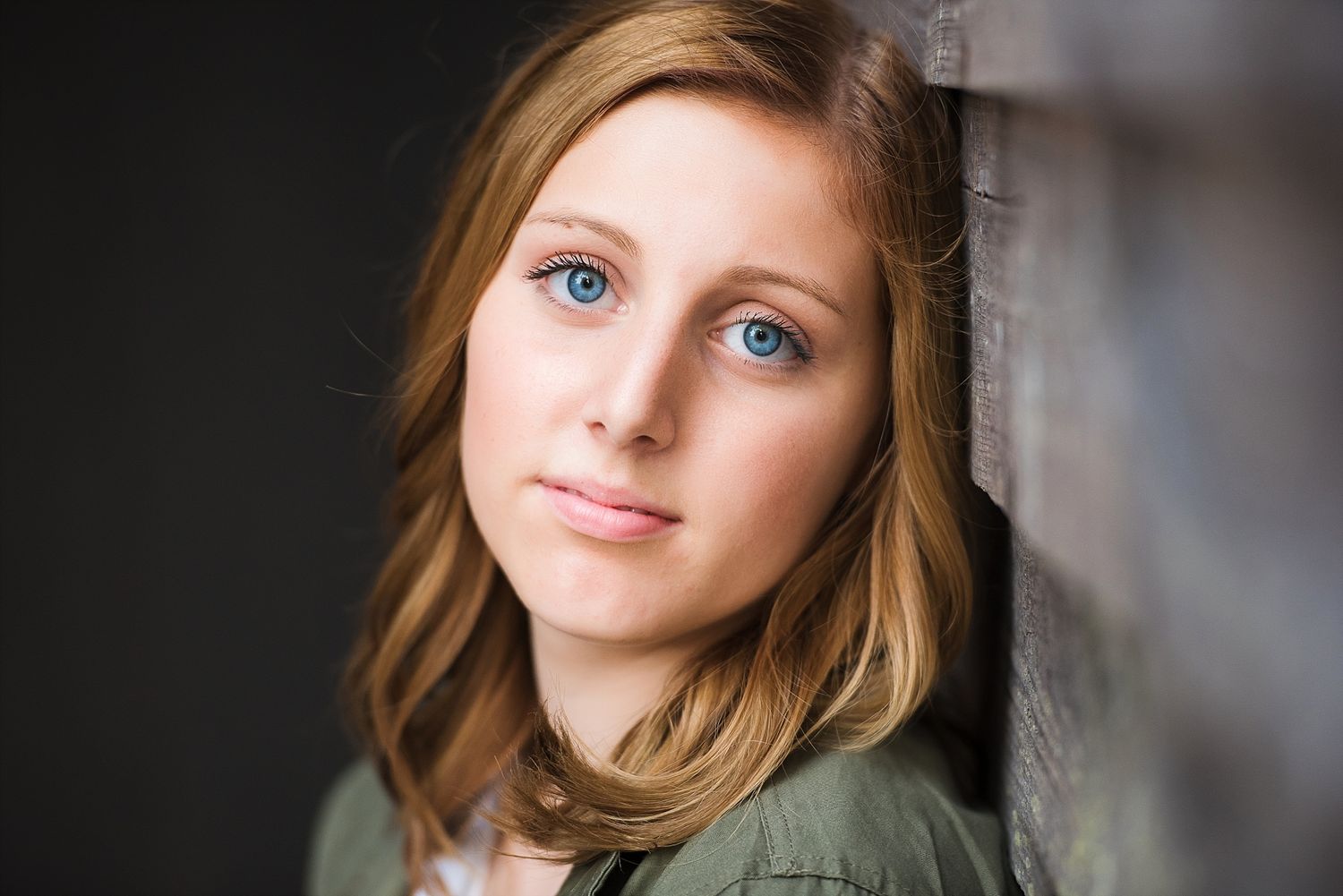 A portrait shot against a dark background highlighting bright blue eyes and natural lighting.