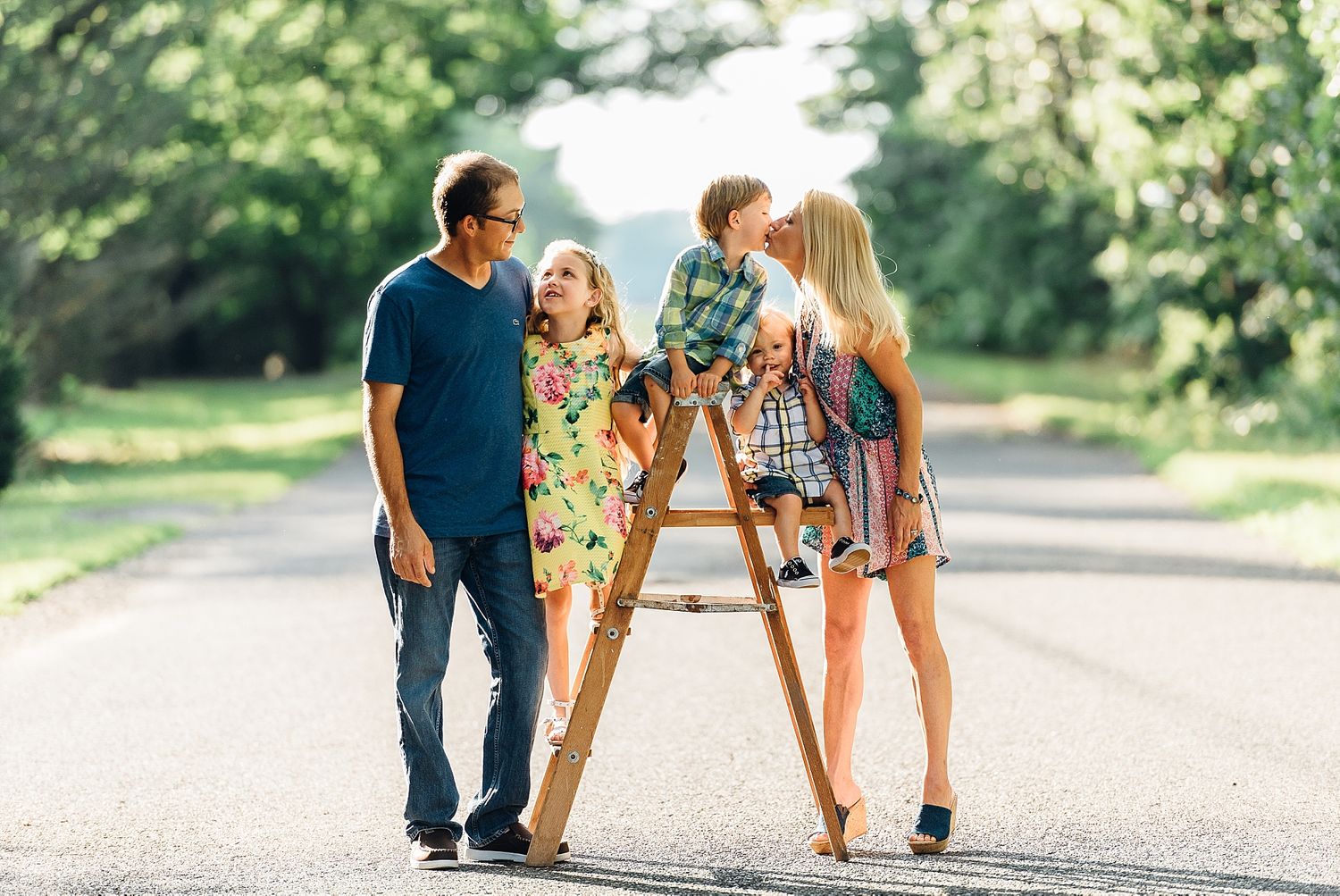 A casual family photo session on a tree-lined path during golden hour.