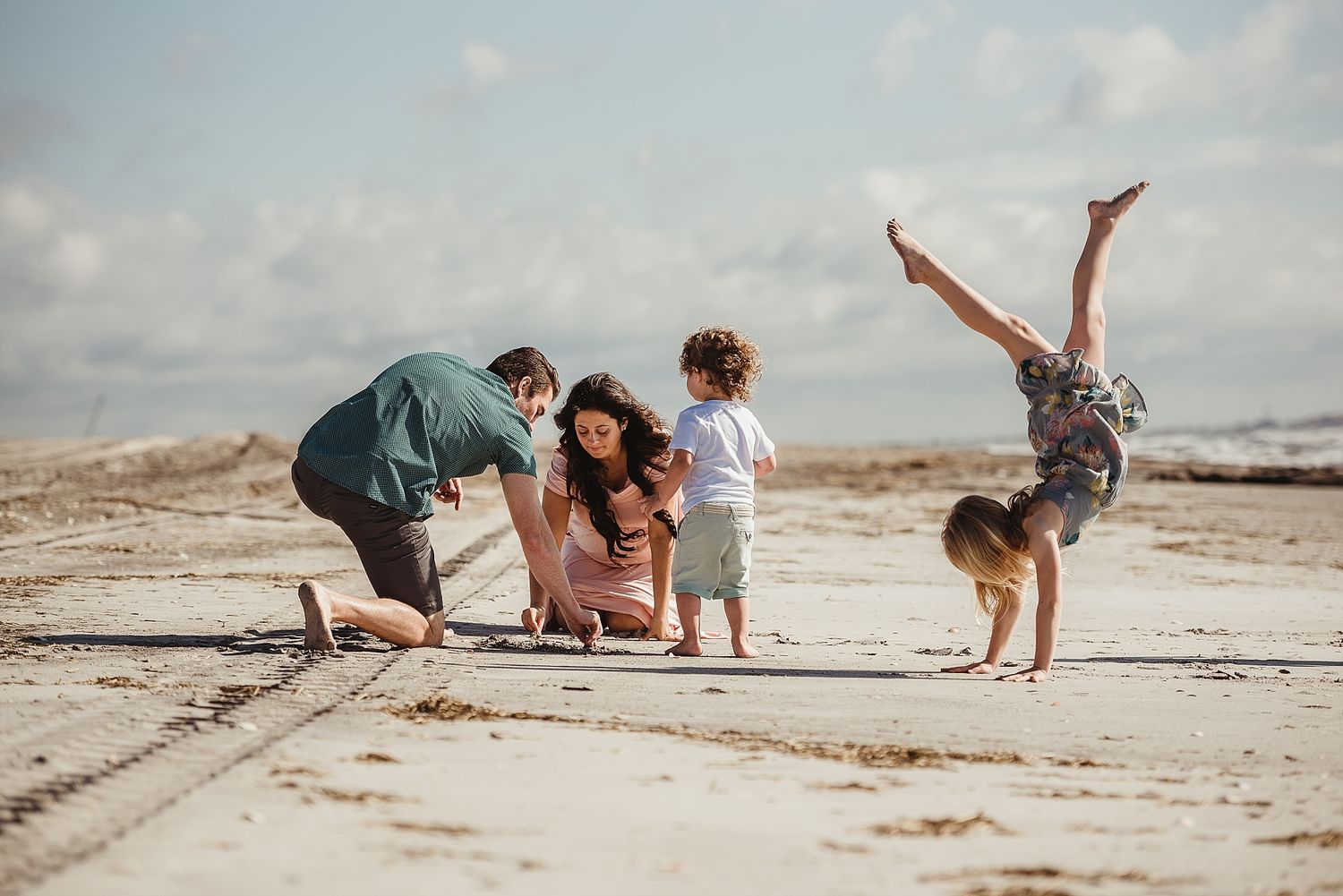 A playful family scene on a sandy beach with someone doing a handstand.