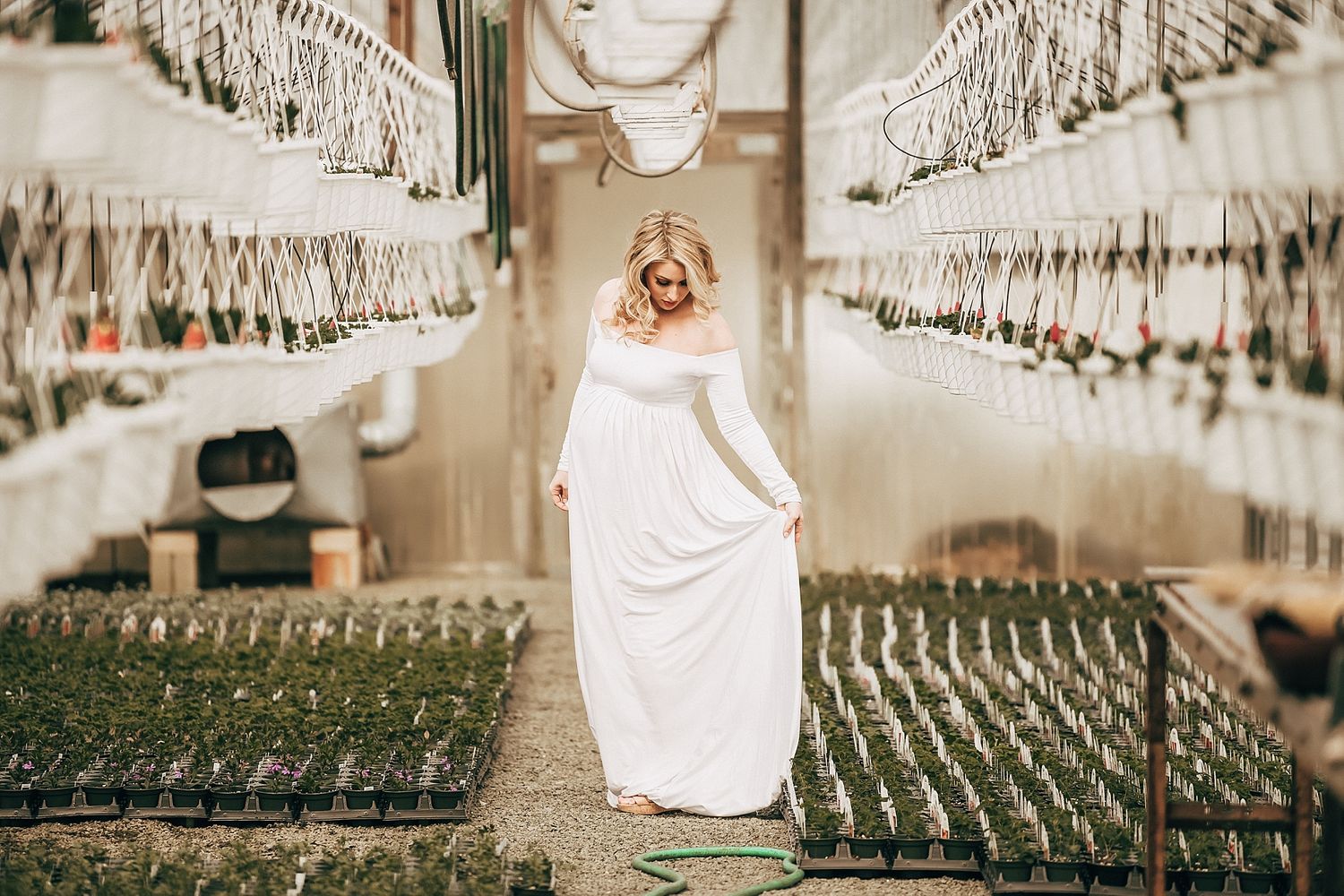 White flowing dress against an artistic greenhouse backdrop with hanging plants.