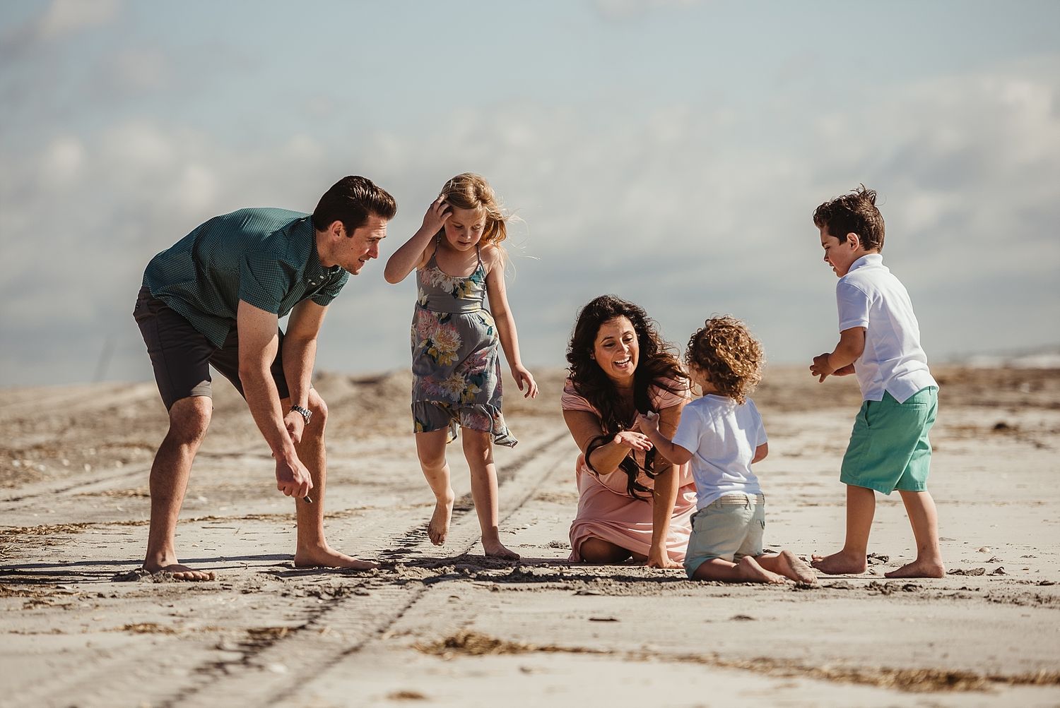 Family playing together on a sunny beach with blue sky and sand.