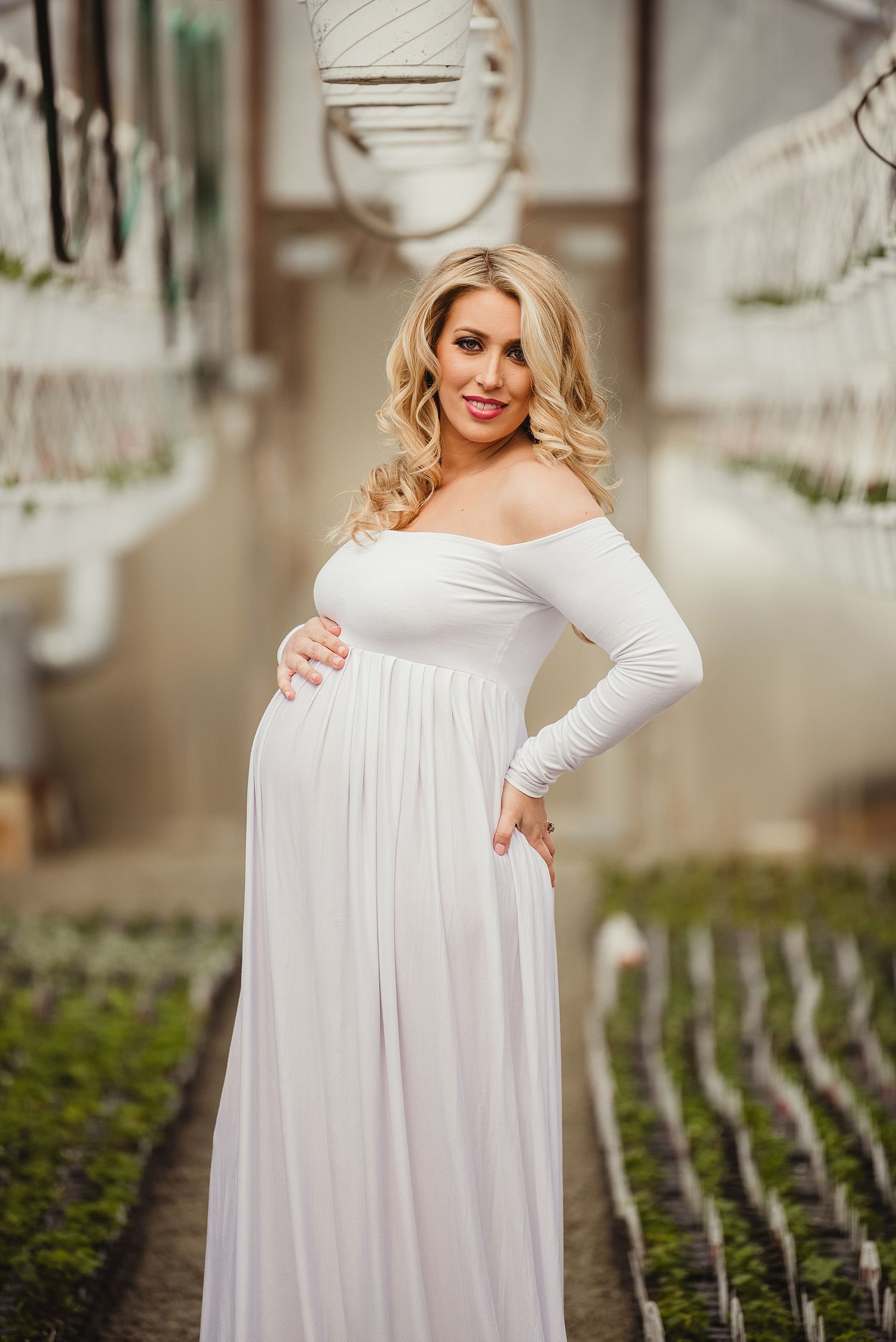 Elegant maternity photo in a greenhouse with white off-shoulder dress.