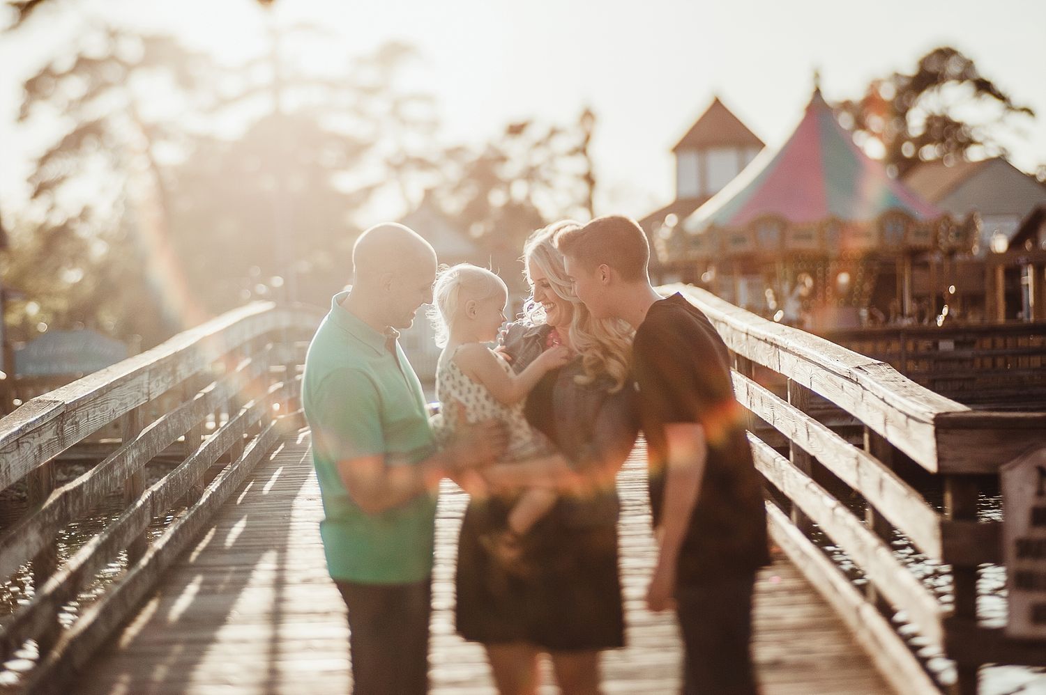 Family gathering on wooden pier at sunset with carnival rides in background.