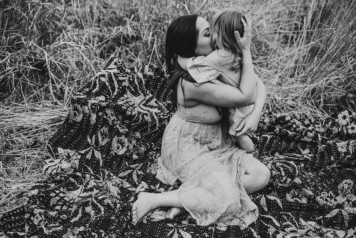 Black and white portrait of tender maternal moment in field of tall grass.
