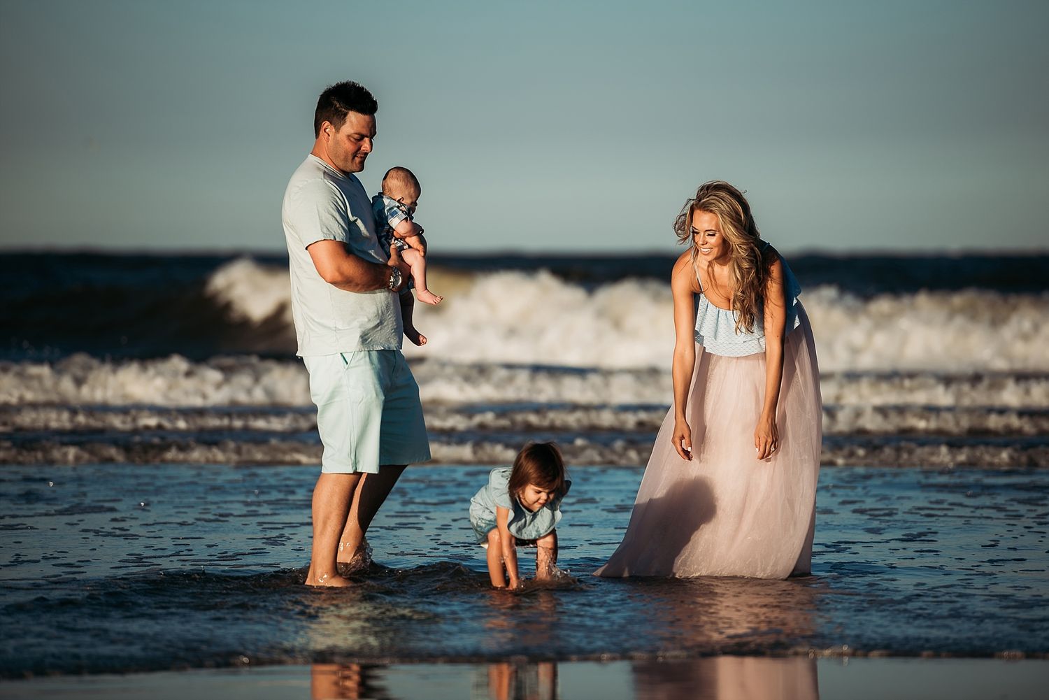 A family plays together at the beach during sunset as waves crash behind them.