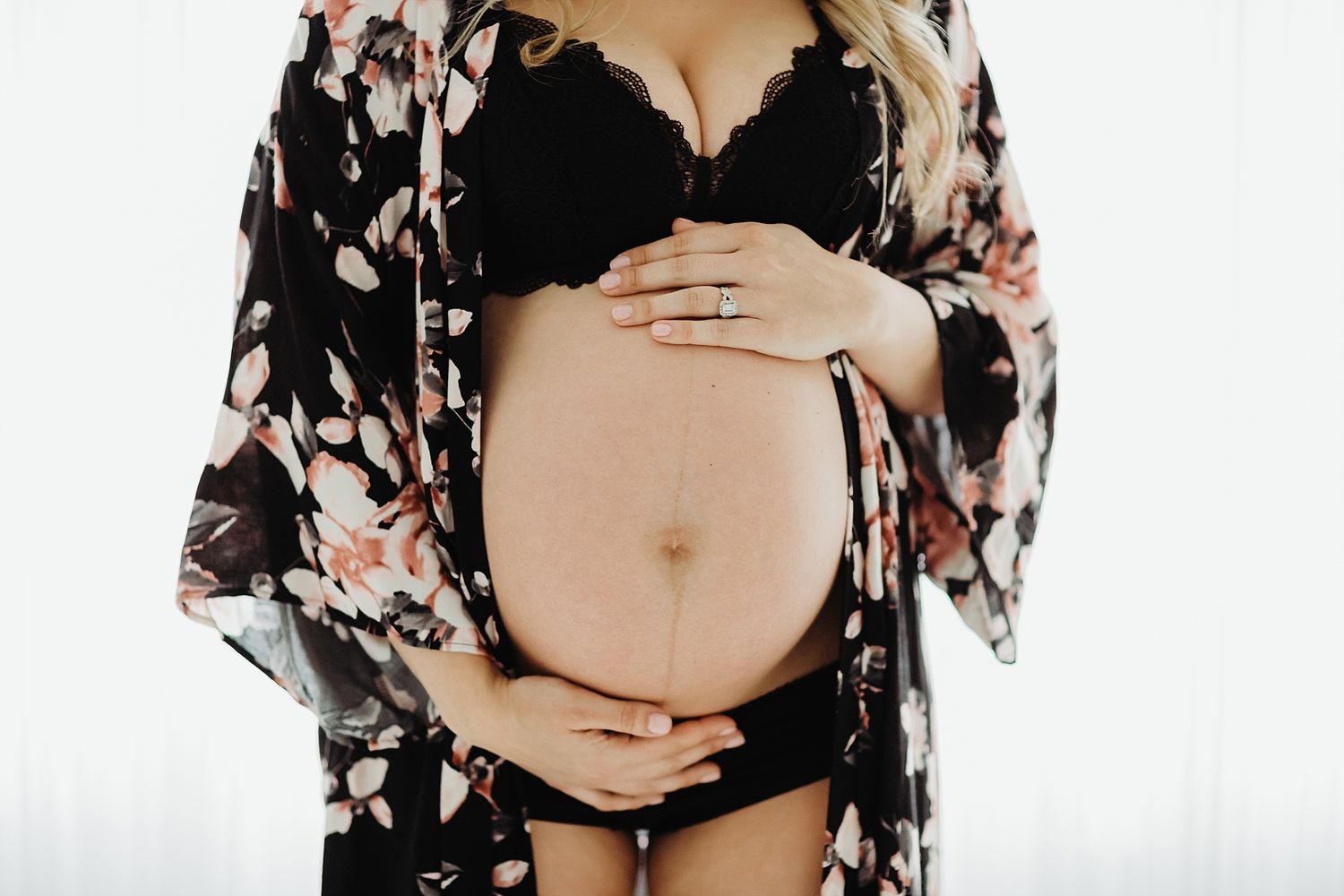 Intimate maternity portrait showing pregnant belly in floral robe against white background.