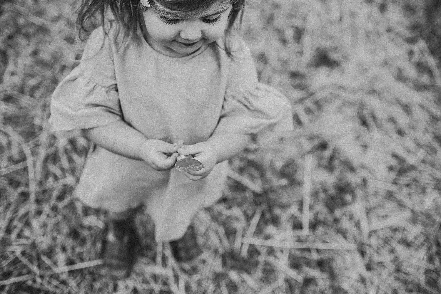 A young child in a dress looking down while playing outdoors in black and white.