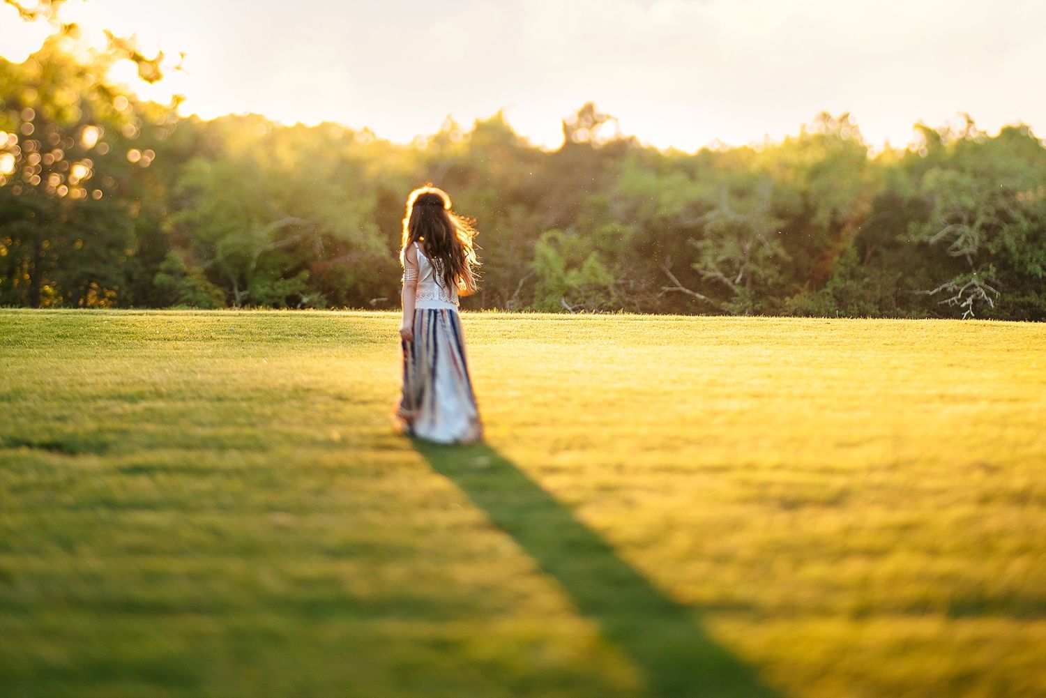 A silhouetted figure stands in a sunlit meadow during golden hour.