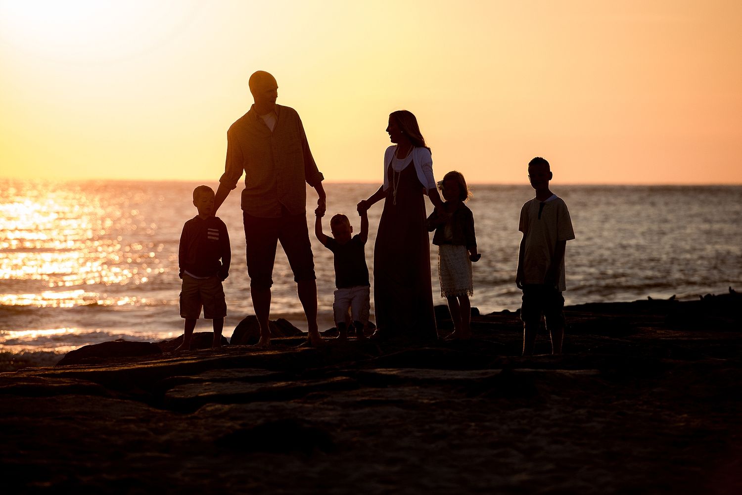 A family of silhouettes stands together on a beach during sunset.