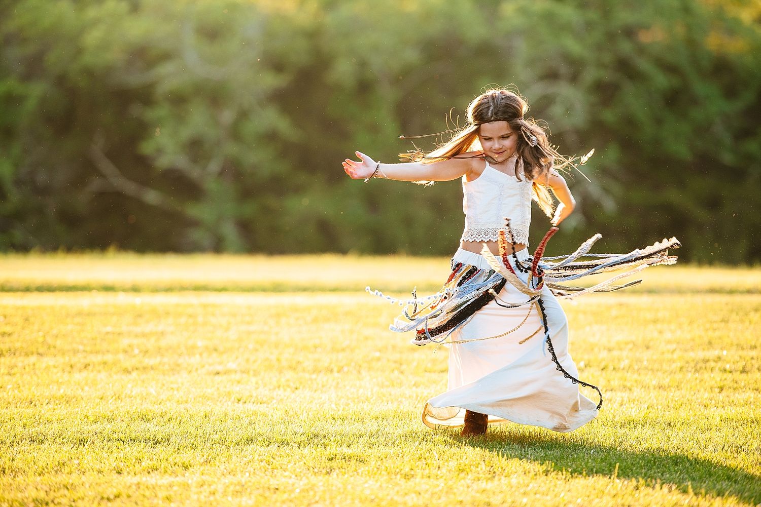 A white dress twirls in motion against a sunlit grassy field during golden hour.