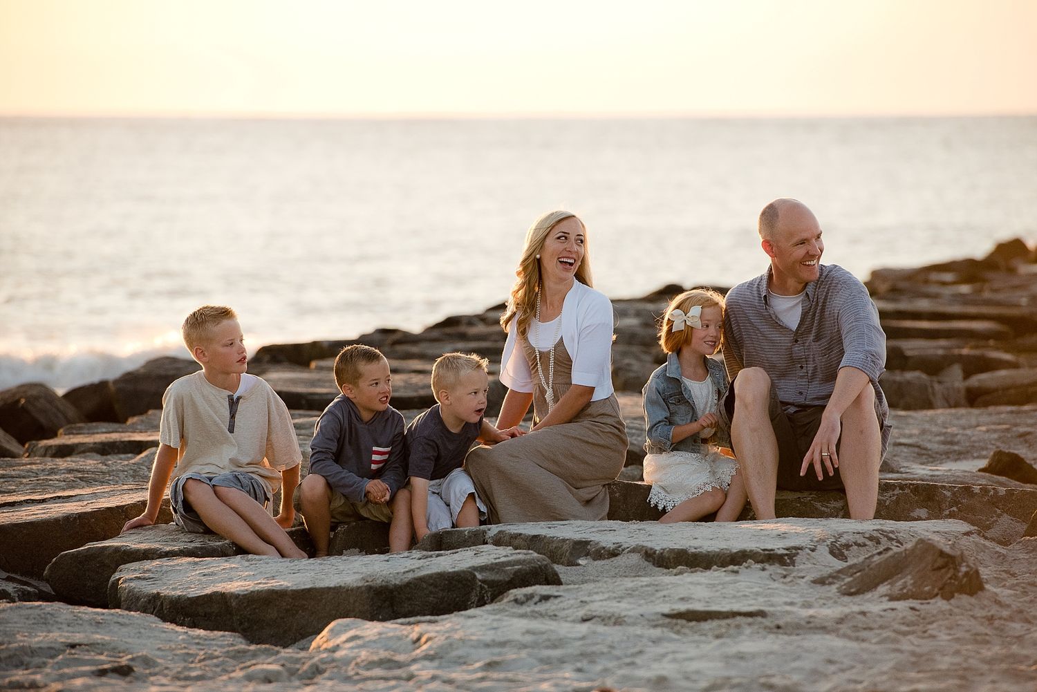 Family sitting together on coastal rocks at sunset by the ocean.