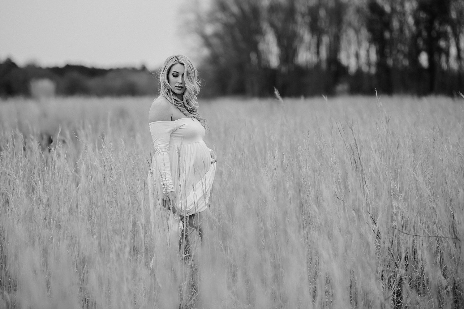 Black and white portrait of figure in white dress standing in tall grass field.