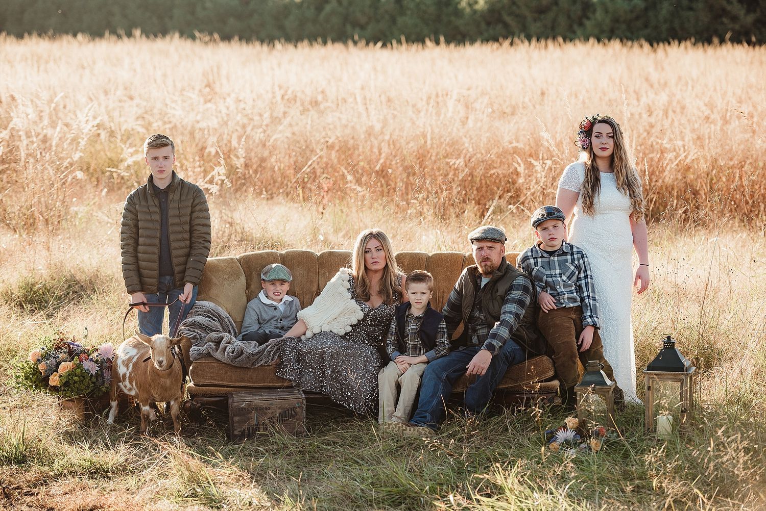 Group lounging on vintage couch in wheat field during golden hour photoshoot.