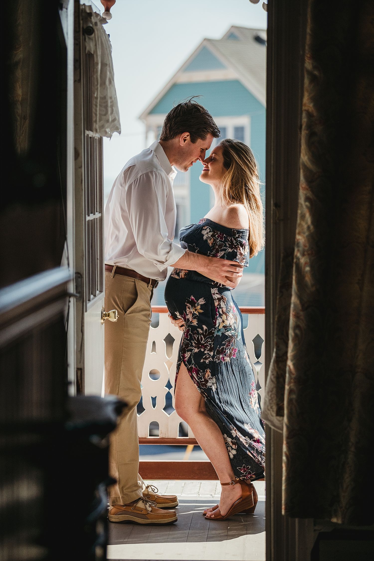 Romantic couple in intimate pose on balcony with teal house in background.