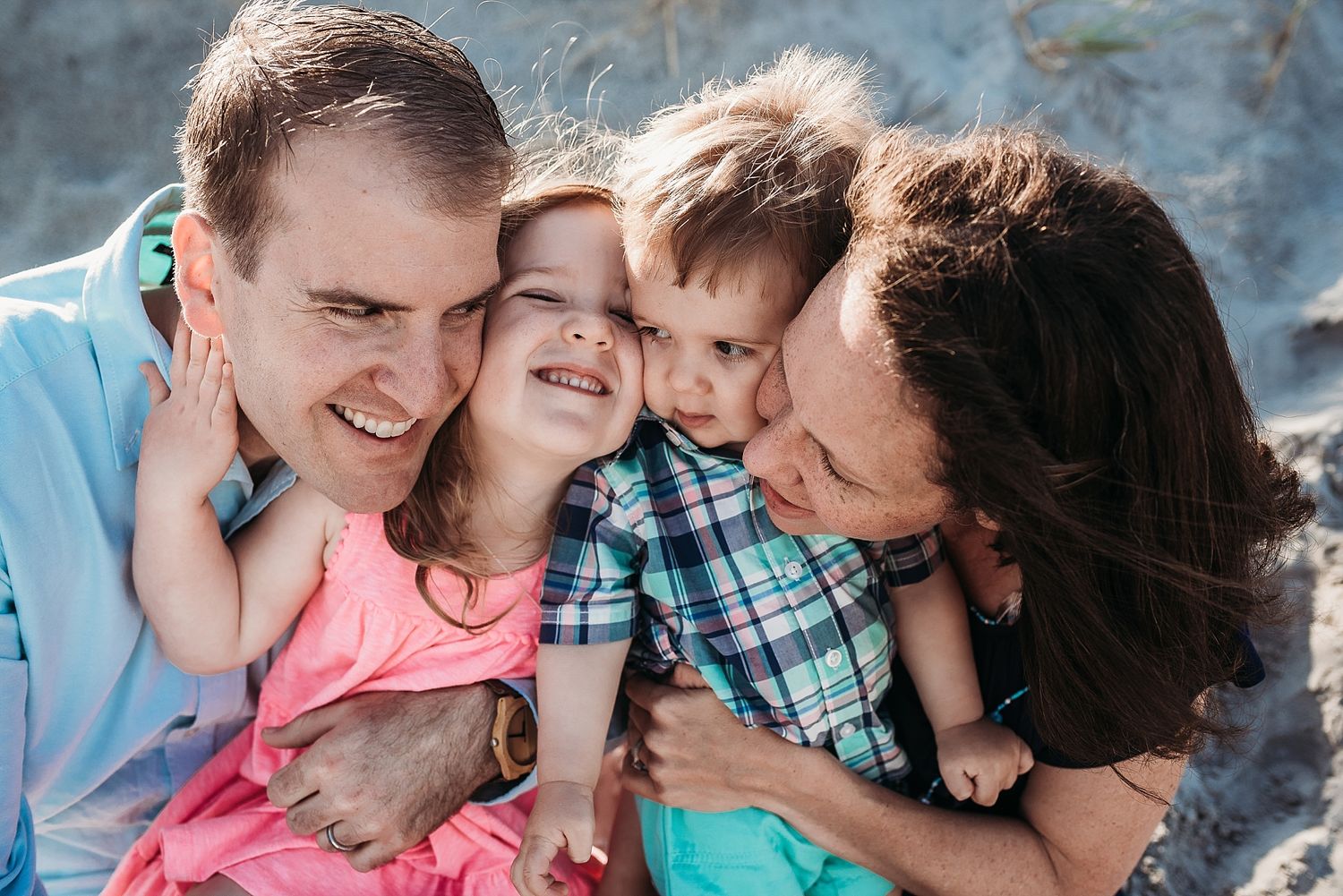 Happy family of four sharing intimate embrace outdoors against stone wall.