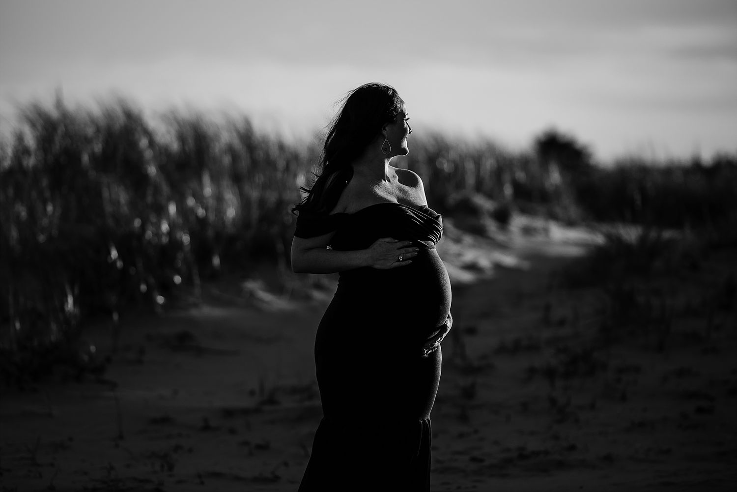 Silhouetted pregnant figure standing on path at sunset.