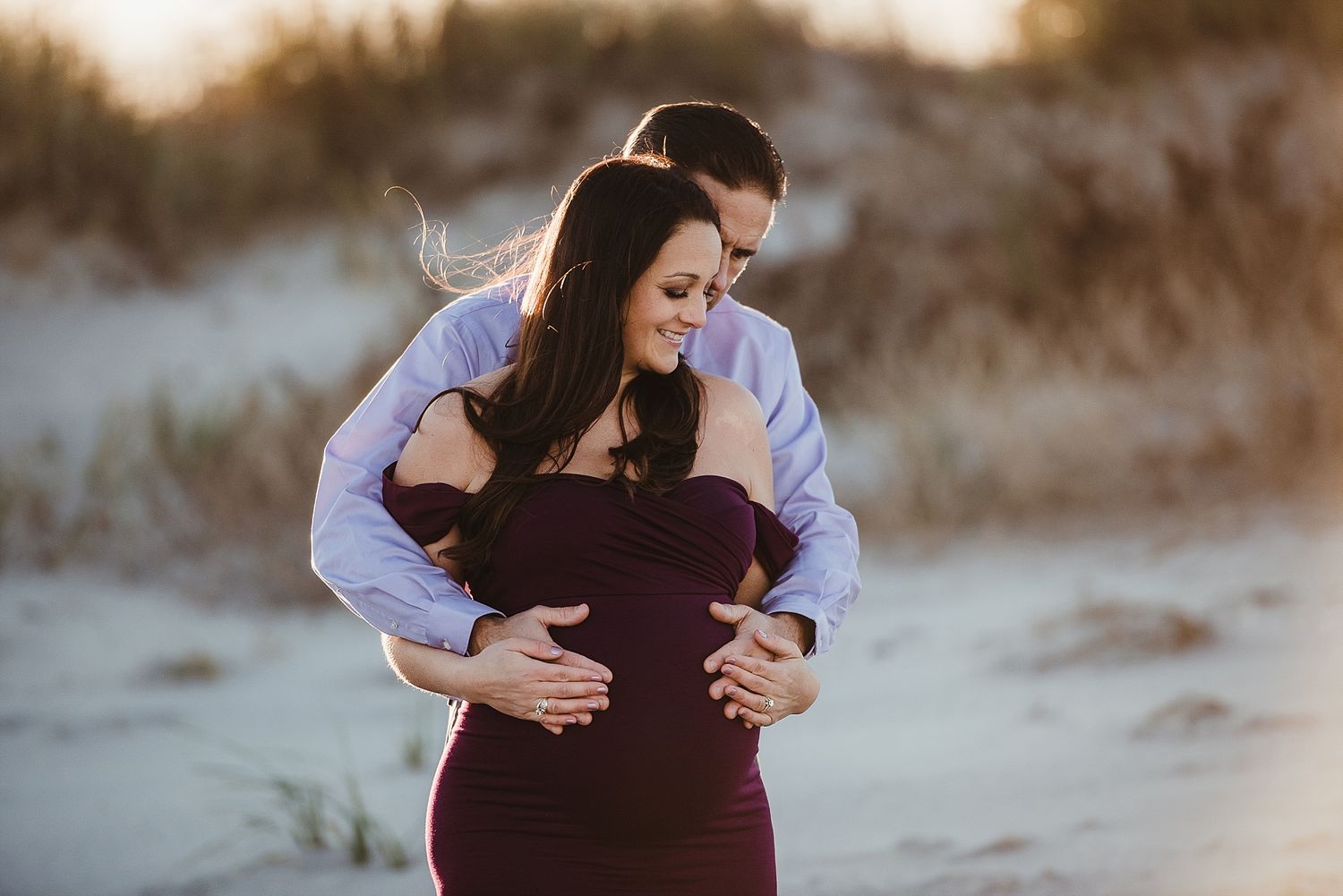 Couple embracing on beach during sunset in intimate maternity pose.