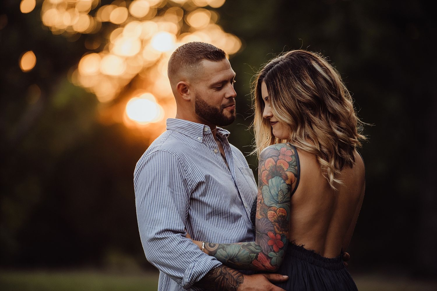 Romantic couple in intimate pose against sunset with bokeh background.