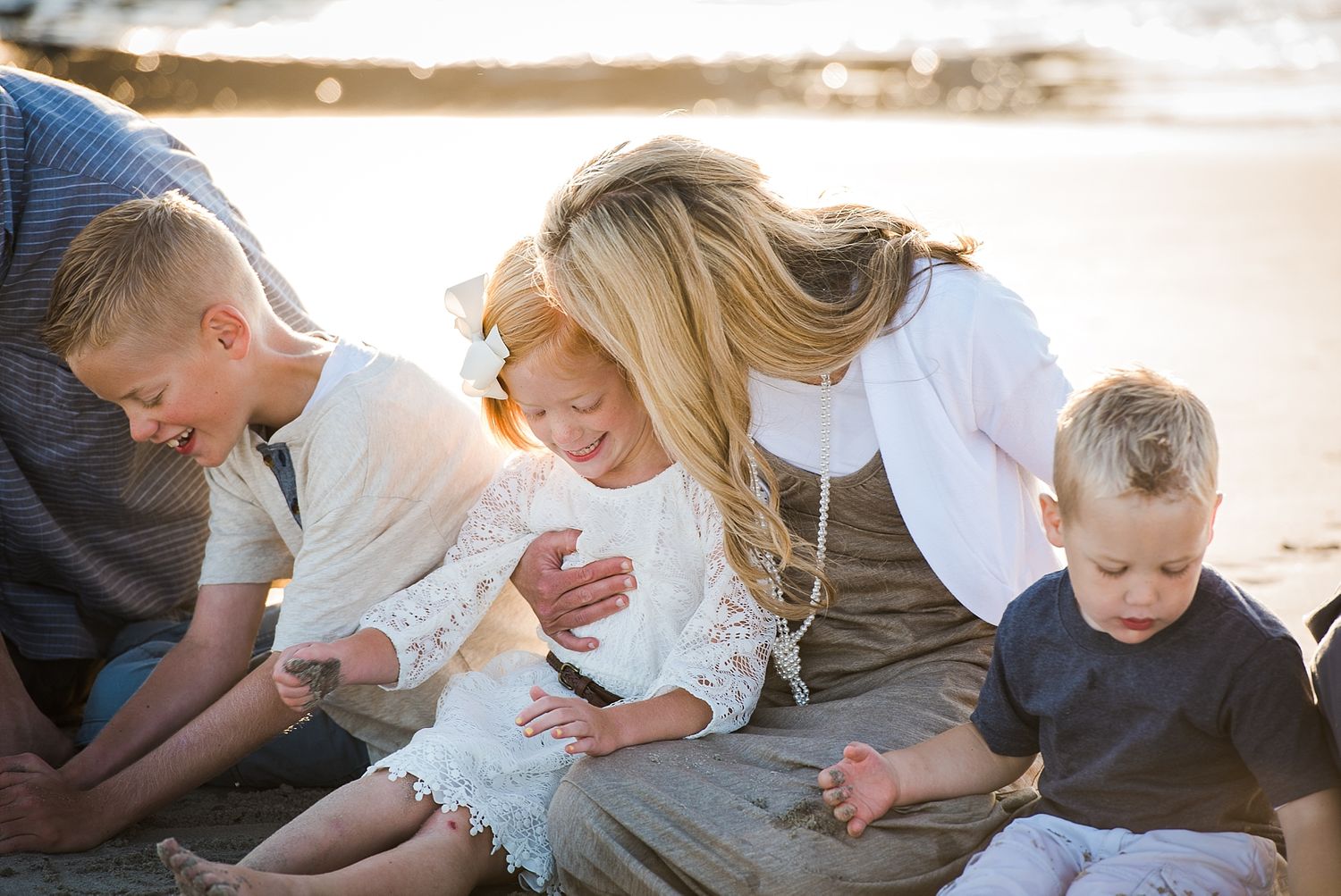 Family shares intimate moment together while sitting on beach at sunset.