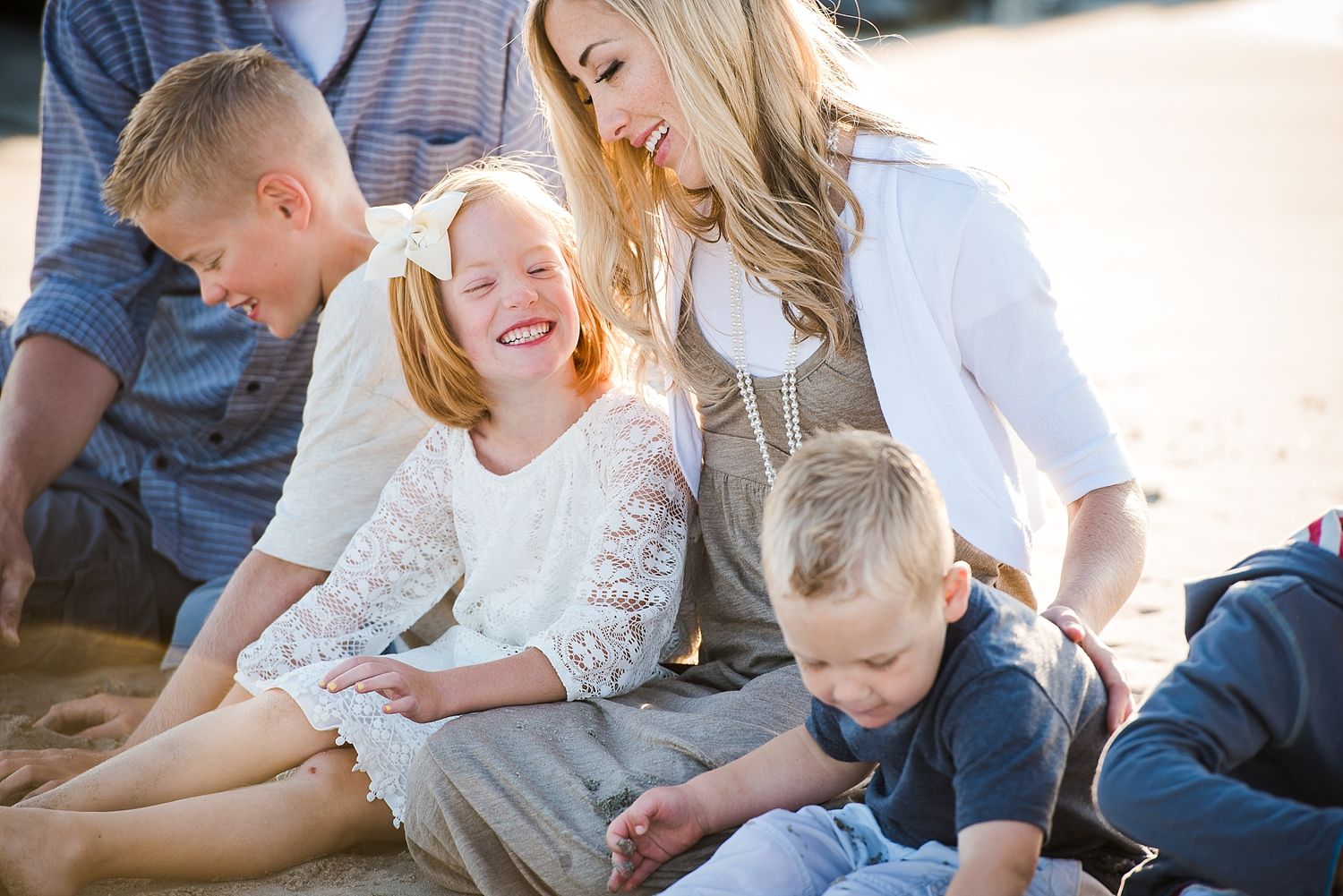 Happy family enjoying playful moments together on sandy beach during golden hour.