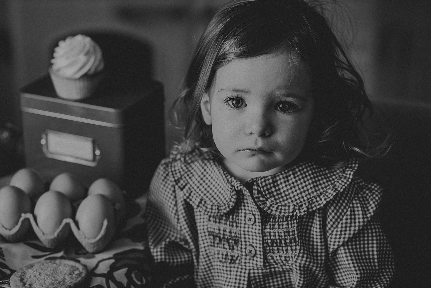 Vintage black and white portrait of small child in gingham dress sitting at table.