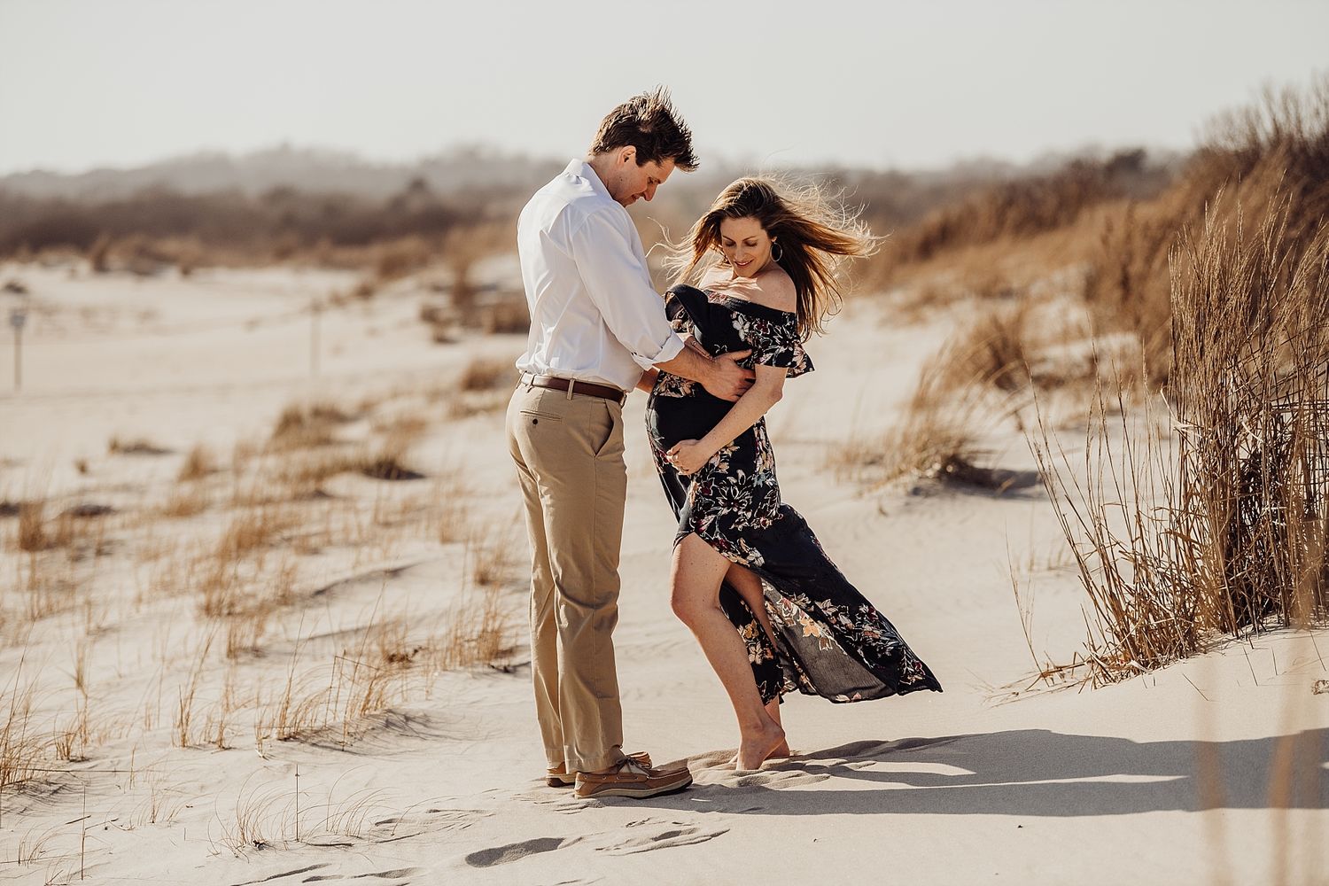 A romantic couple dancing and embracing on sandy dunes during a warm sunset photoshoot.