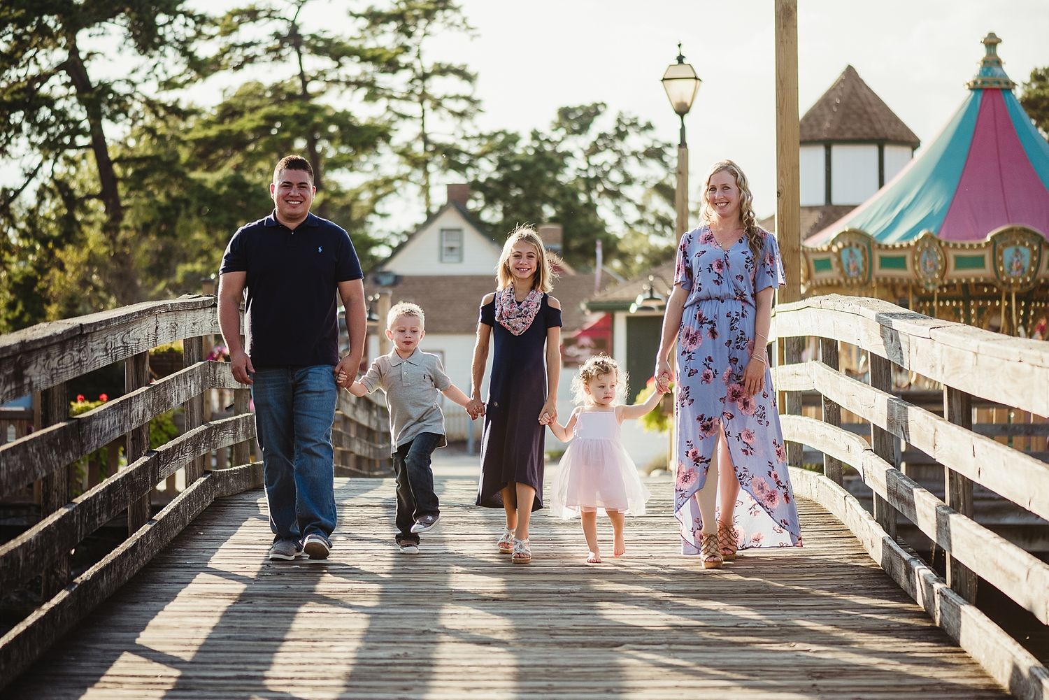 A family walks together on a wooden boardwalk with an amusement park in the background.