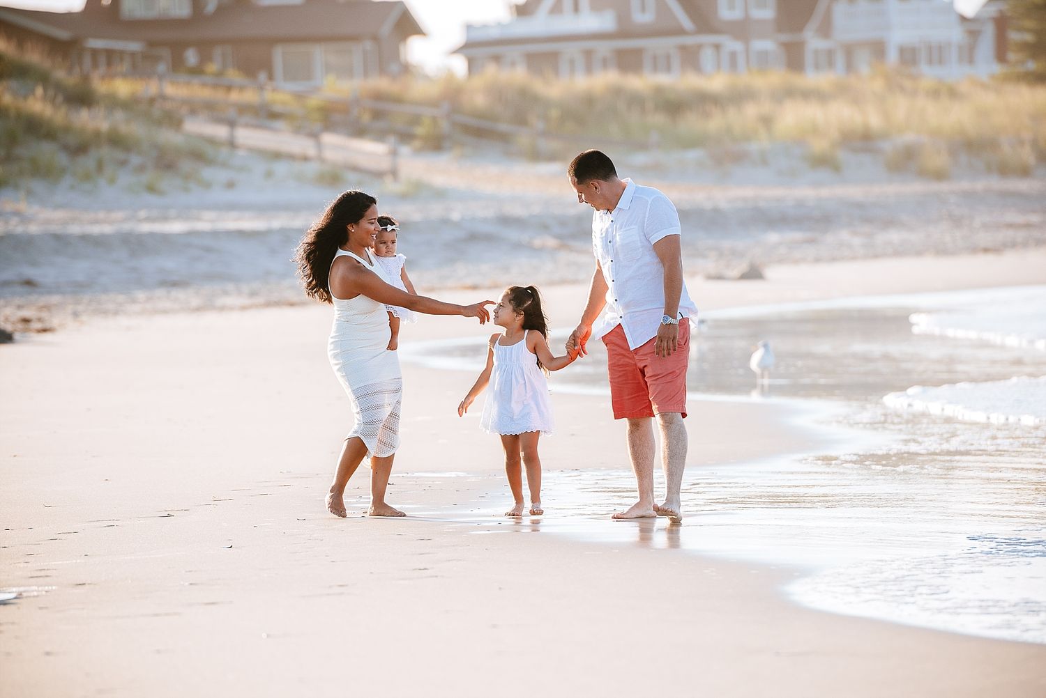 A family walking hand in hand along a beach at sunset with beachfront homes in the background.