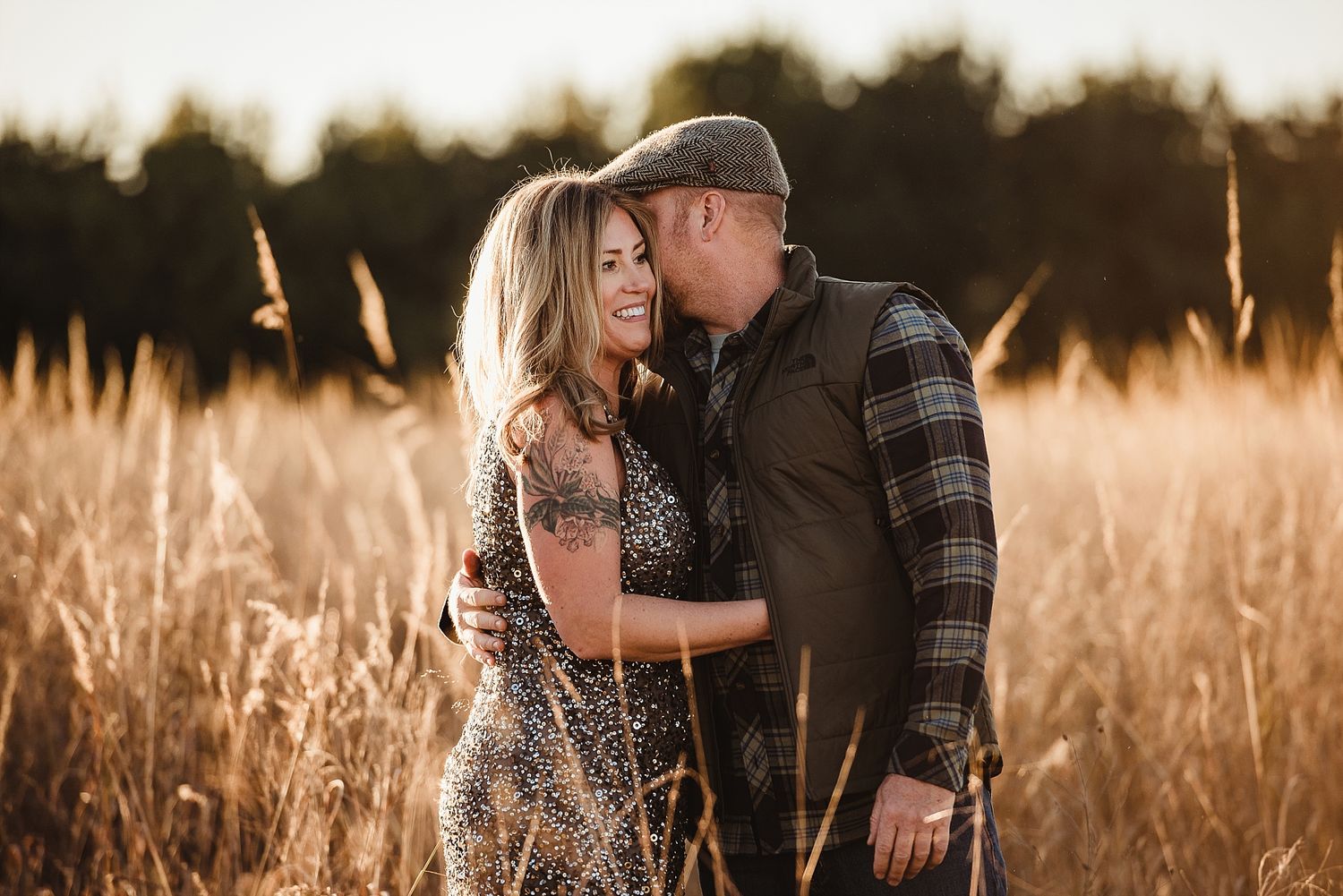 A romantic couple embraces in a sunlit field of tall golden grass during golden hour.