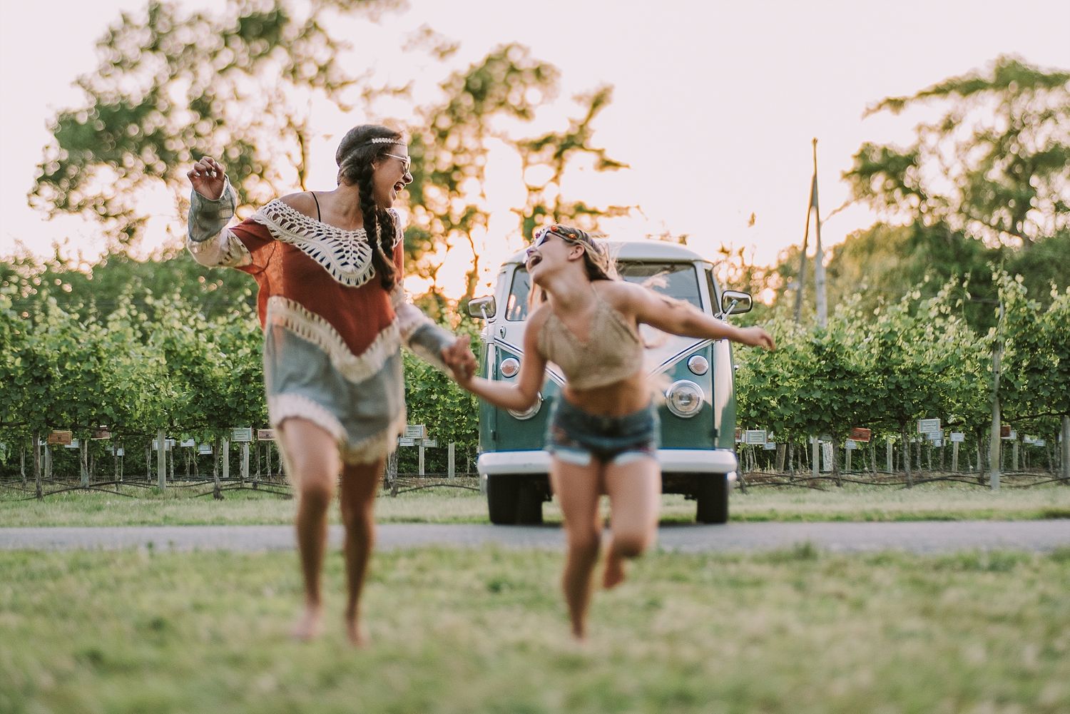 Two people run and play in a grassy field with a vintage vehicle parked in the background.