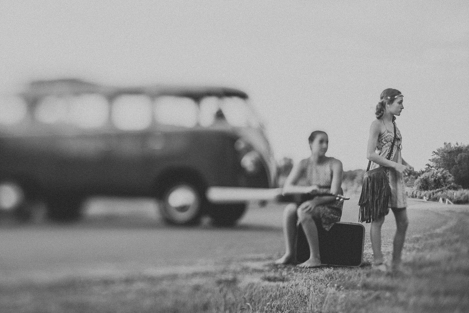 A vintage black and white scene with figures silhouetted against an old car on a hill.