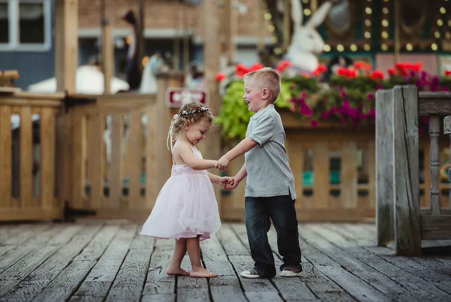 Two small children dance together on a wooden deck decorated with string lights.