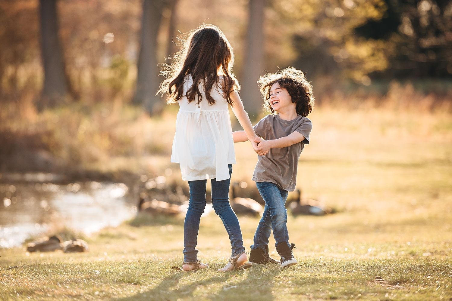 Two children dance and play together in a golden sunlit field during autumn.