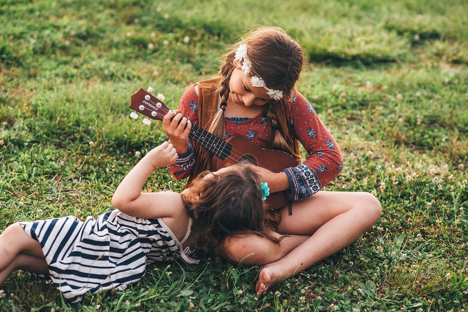 Two people relaxing on grass while one plays ukulele on a sunny afternoon.