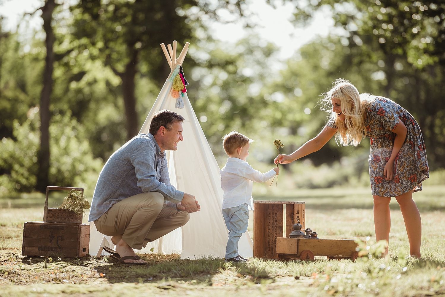 Family playing with teepee tent and boxes in sunny backyard setting.