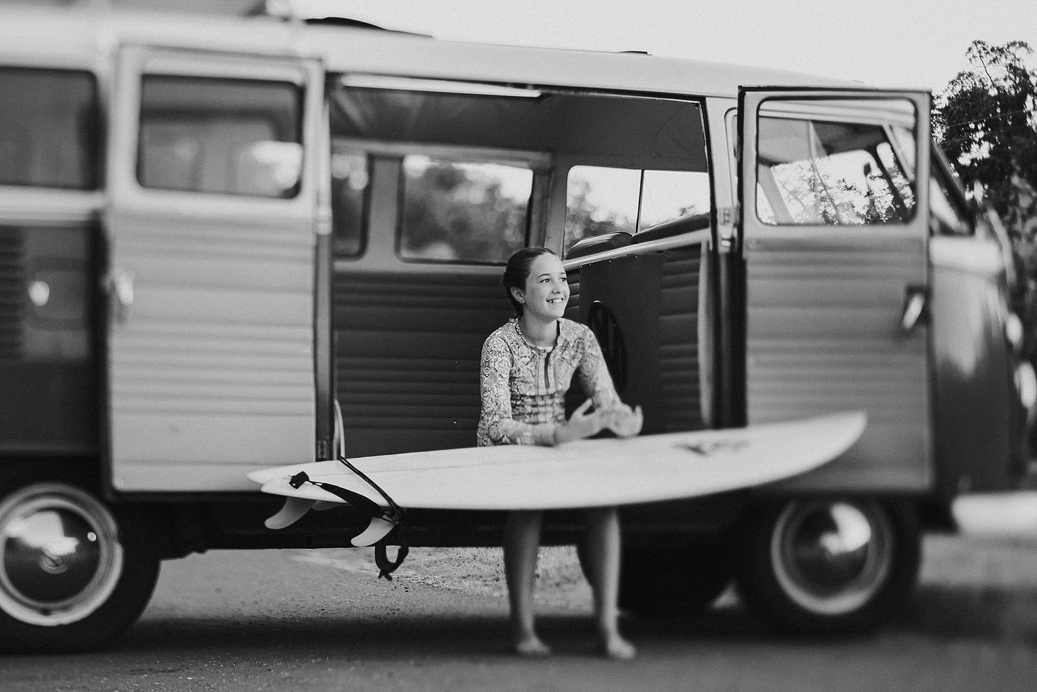 Person sitting in vintage VW van with surfboard in black and white.
