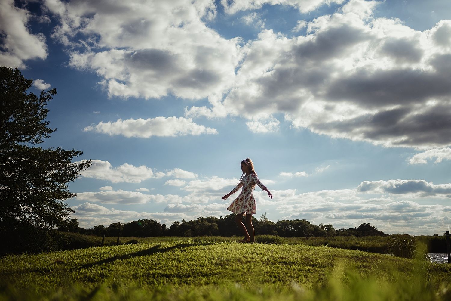 A silhouetted figure leaps joyfully on a grassy hill against a dramatic cloudy sky at sunset.