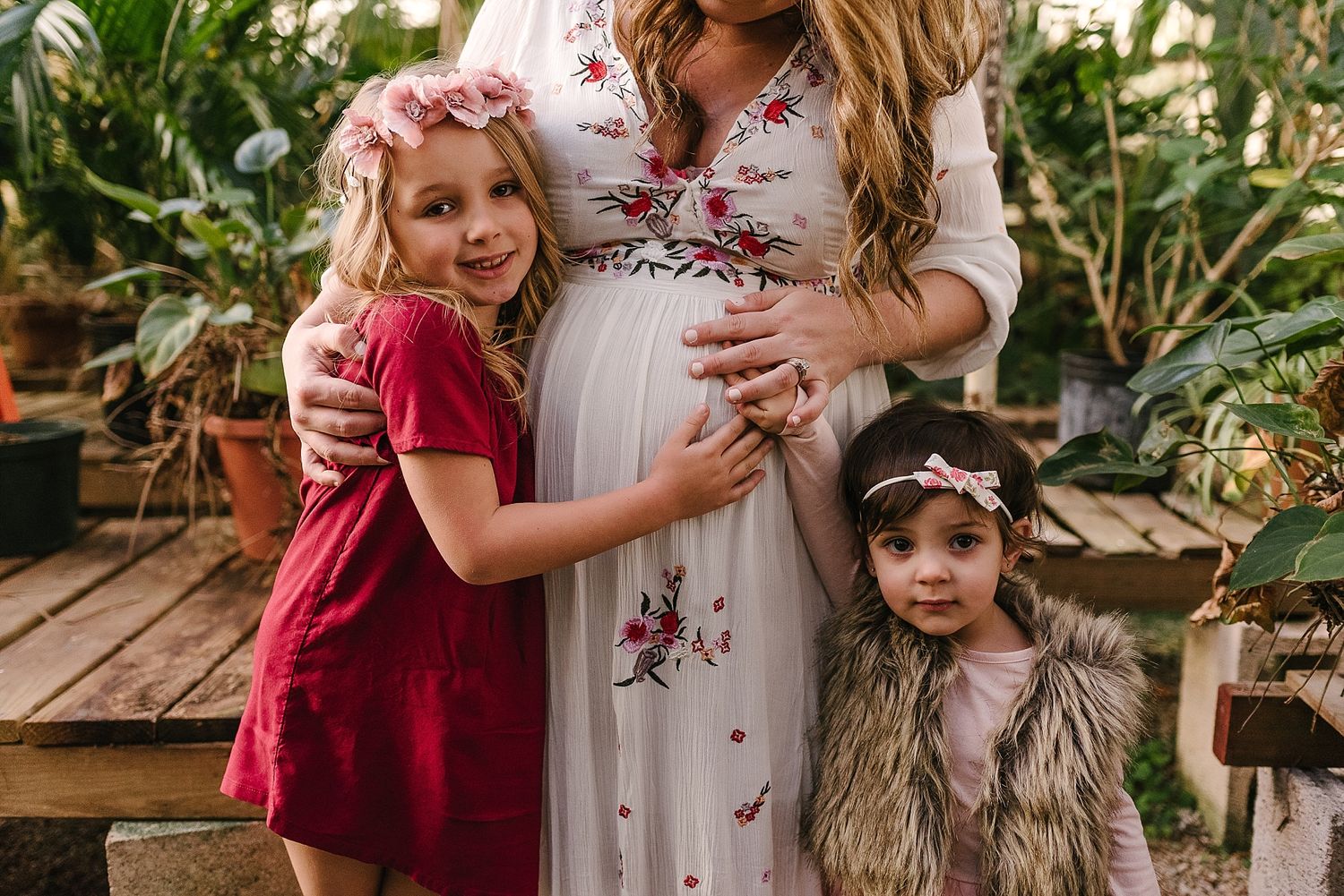 A maternity moment captured on wooden steps surrounded by greenery in a garden setting.
