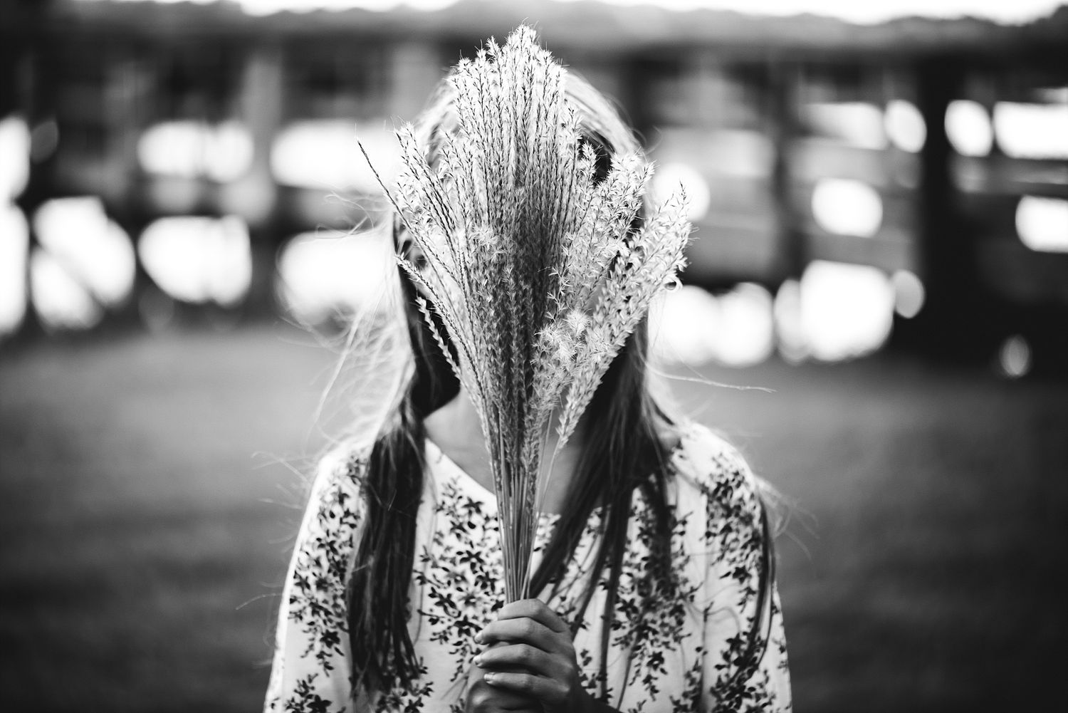 Artistic black and white portrait of someone holding a feathery pampas grass in front of their face.