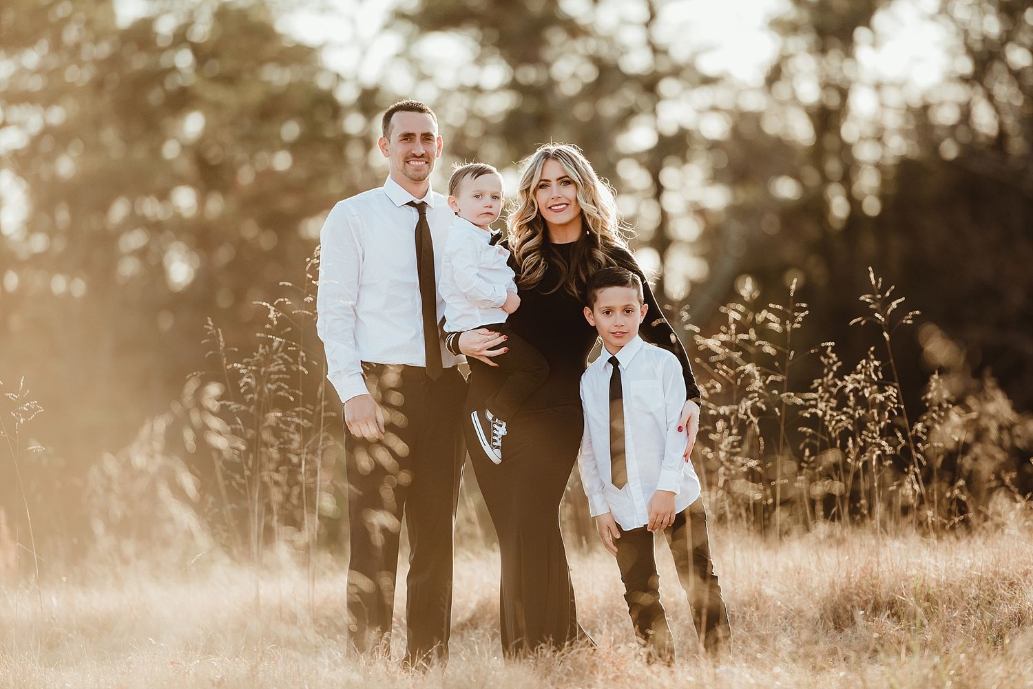 A family portrait in warm golden light with pine trees in the background.