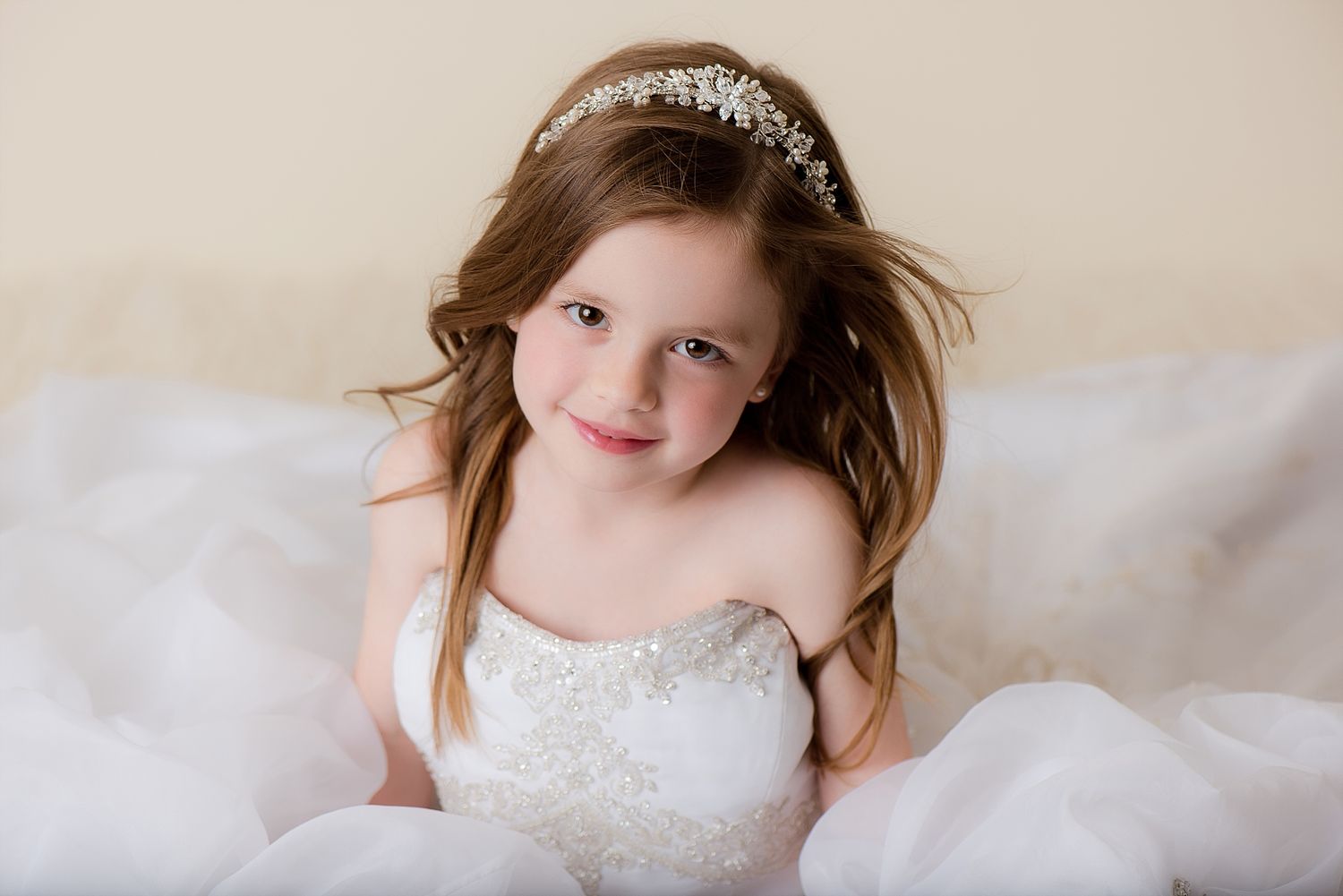 A magical portrait of someone wearing a sparkly white dress and tiara against soft white pillows.