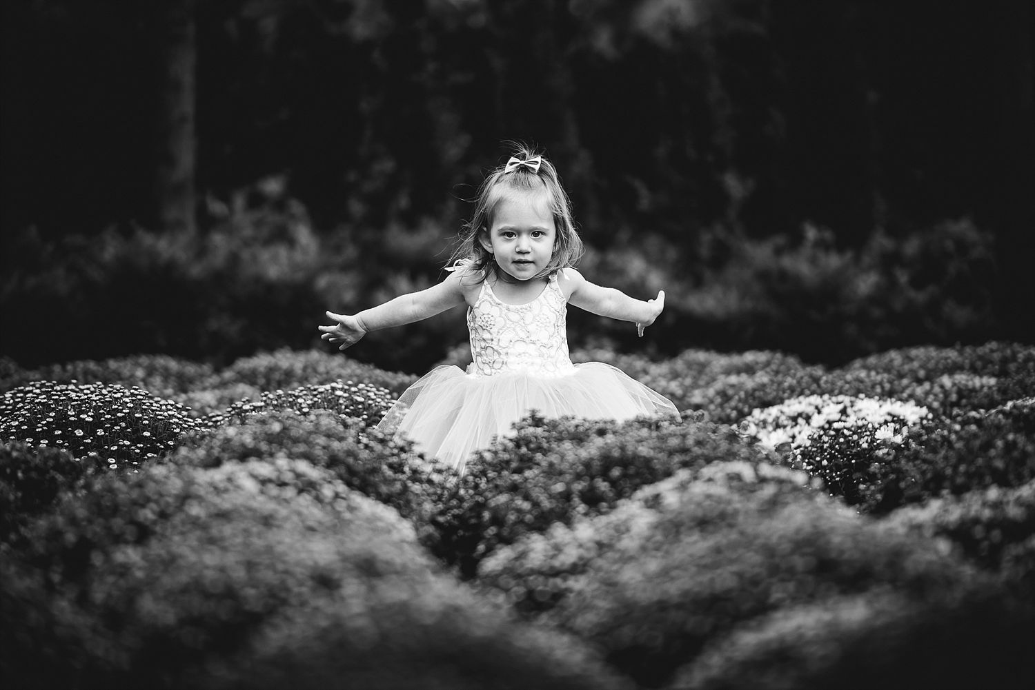 A black and white image showing a figure in white emerging from lush garden foliage.