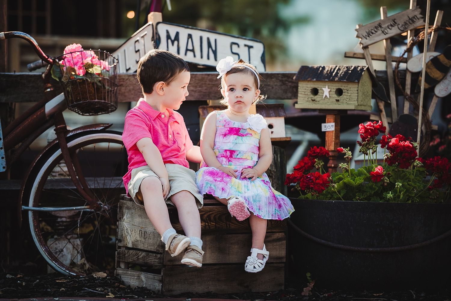 Two people sit together on a rustic Main Street bench surrounded by flowers and birdhouses.