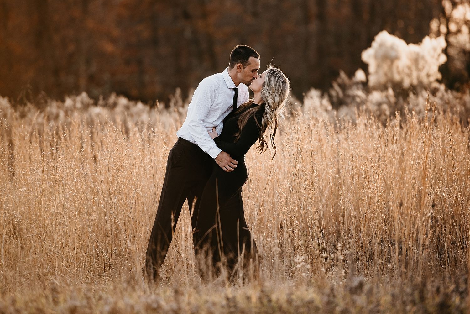 A romantic couple embraces in a field of tall golden grass at sunset.